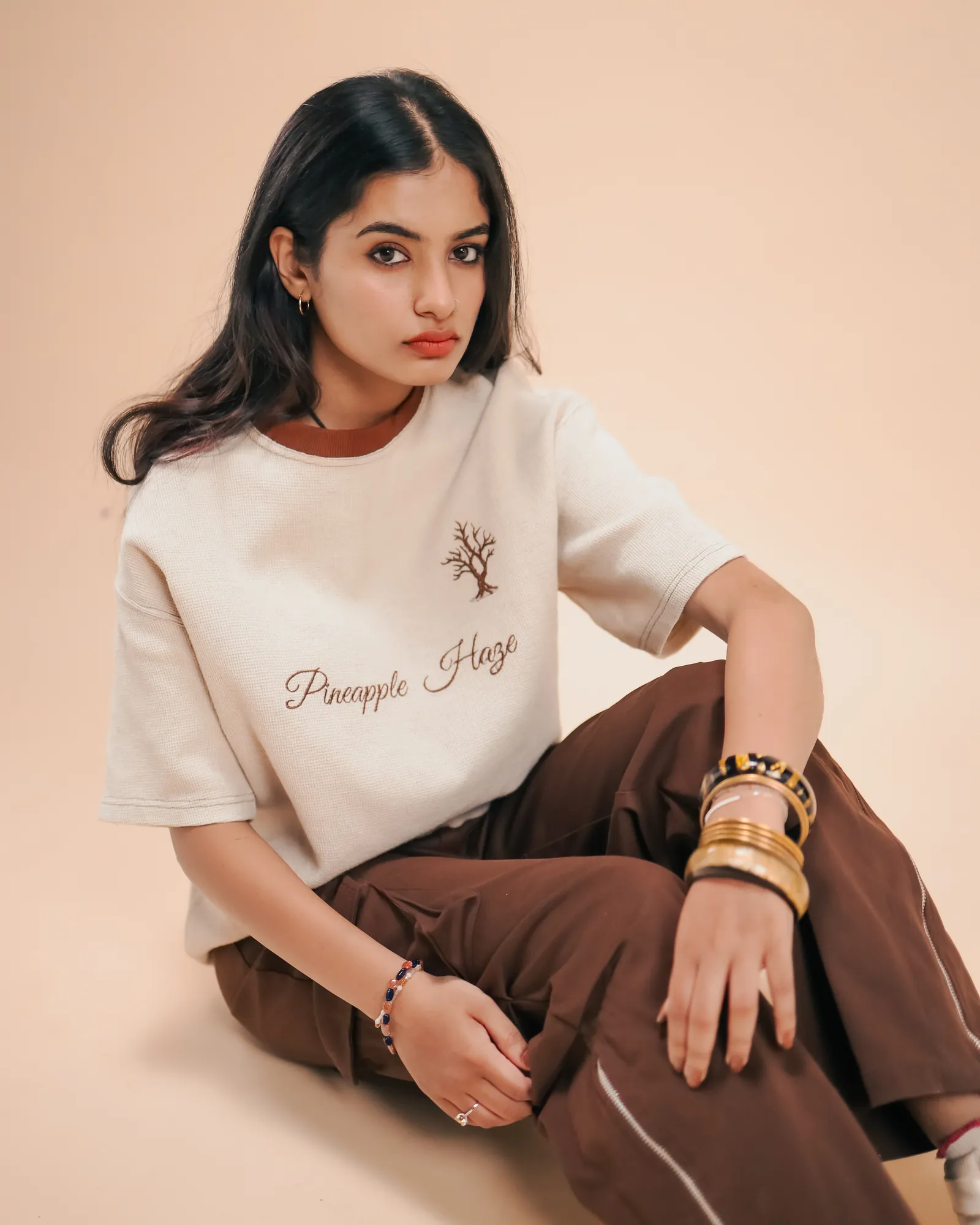 Sitting on the studio floor in the Pineapple Haze tee and brown cargo trousers